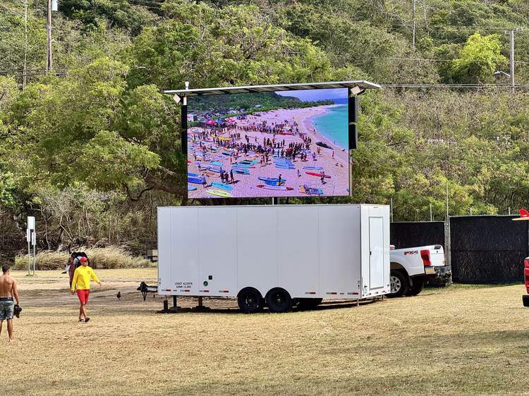 TV1 mobile LED trailer showing a live aerial feed of a paddle-out ceremony